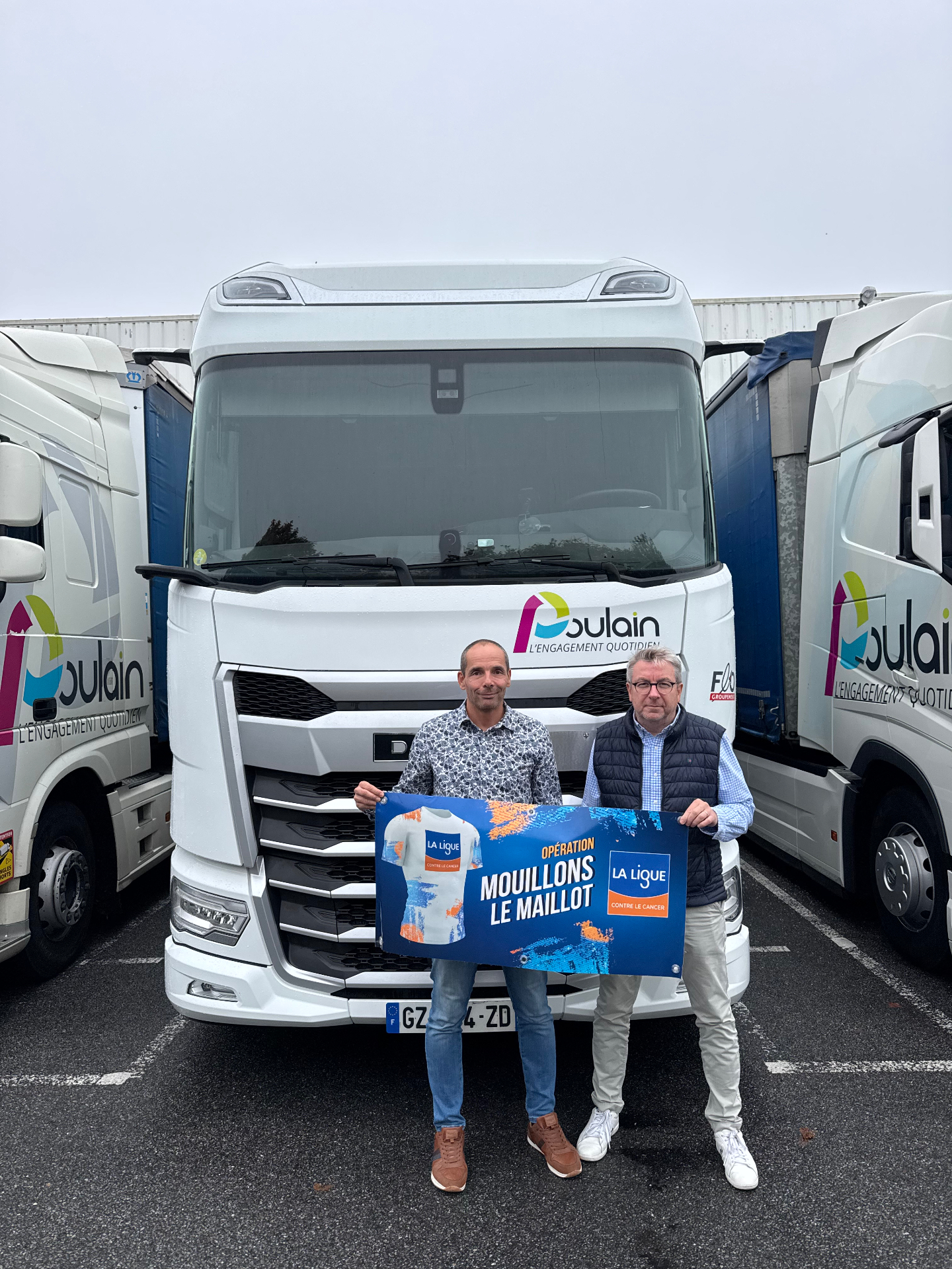 Les Transports Poulain soutiennent l'opération "Mouillons le Maillot" Deux collaborateurs des Transports Poulain devant un camion DAF, tenant le panneau solidaire de l'opération Mouillons le Maillot pour la Ligue contre le cancer