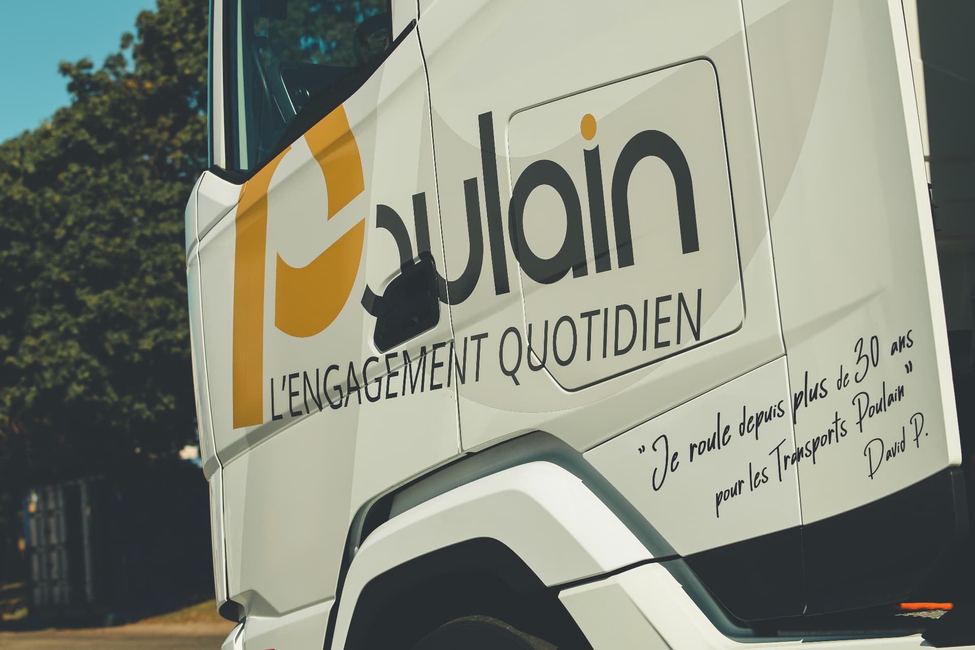 Gros plan de profil sur la cabine blanche DAF XG avec le logo Poulain jaune et noir, décor 60 ans